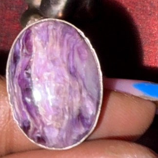 Short description: A handcrafted sterling silver ring set with a swirling purple charoite oval cabochon on an engraved floral band. One of a kind, size 9.